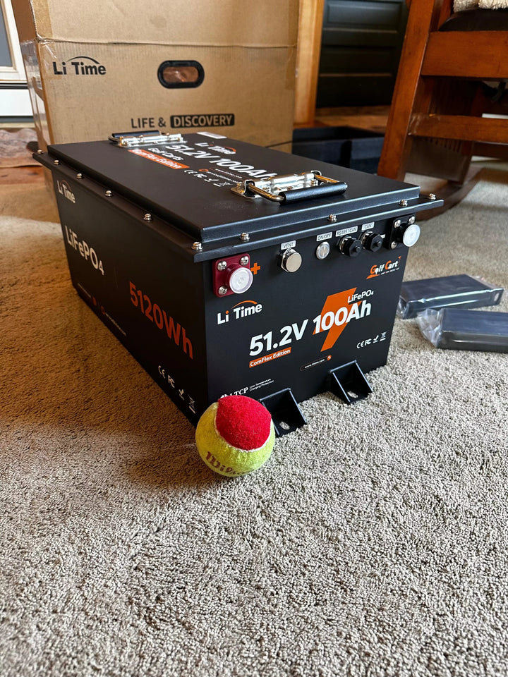 A LiTime 51.2V 100Ah battery is placed on carpet, showcasing its features alongside a tennis ball for scale, in a customer review