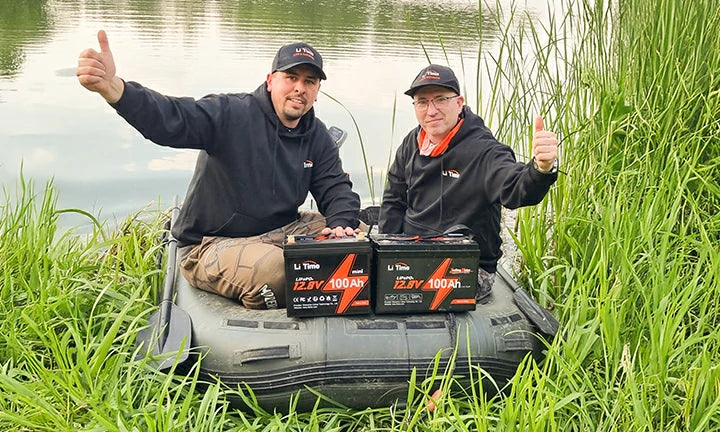 Two men give a thumbs-up while sitting in an inflatable boat on a grassy bank with two LiTime batteries
