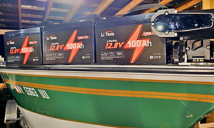 A lineup of four LiTime 100ah trolling motor batteries installed inside a green boat.