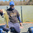 A smiling fisherman in a LiTime t-shirt kneels on a boat, holding up a freshly caught bass